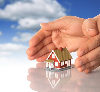 Hands and little house over sky background.